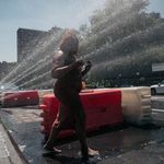 Tameka Jones steps through an opened fire hydrant on Broadway in West Harlem on Saturday, July 23rd.